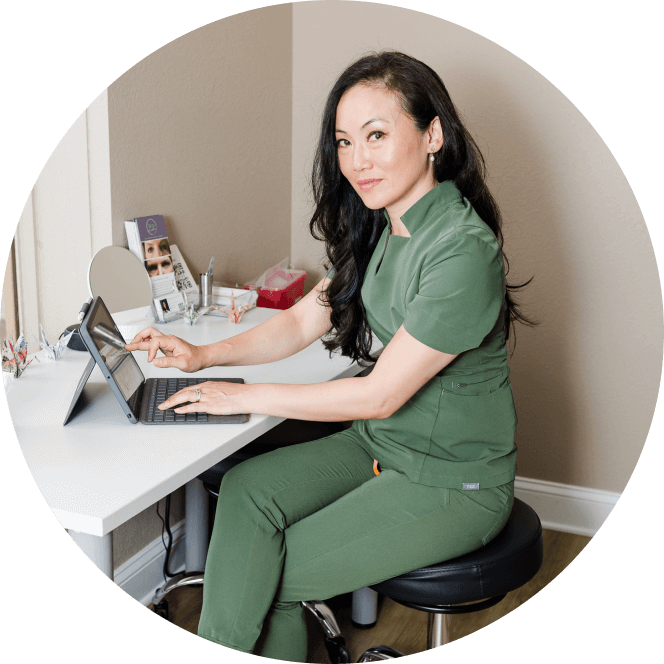 Dr. Choe, dressed in green scrubs, is at her desk with a laptop, concentrating on her work in a medical setting