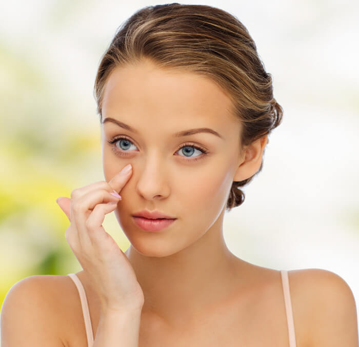 A woman with striking blue eyes touches her face thoughtfully, reflecting a moment of introspection